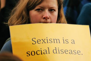 Woman holding sexism is a social disease sign Woman holding sexism is a social disease sign