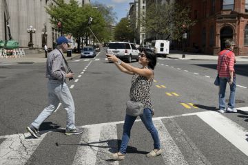 Woman using smartphone selfie stick while crossing road Woman using smartphone selfie stick while crossing road
