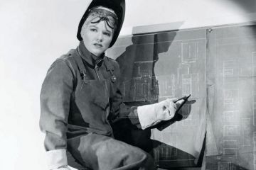 Woman wearing protective clothing pointing at blueprints Woman wearing protective clothing pointing at blueprints