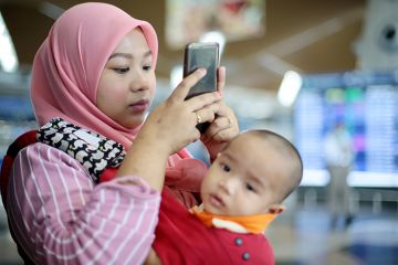A woman with a baby looking at her phone at an airport. To illustrate that online marketing to prospective international students states that they would be eligible to bring family members with them, despite the UK government’s dependants visa ban.