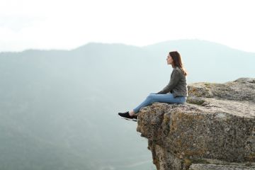A woman sits on the edge of a cliff