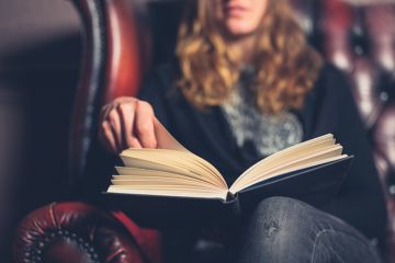 A woman reading in an armchair illustrating book reviews, best books of the month