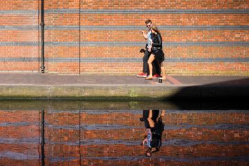 Young couple walking along canal with reflection on water Young couple walking along canal with reflection on water