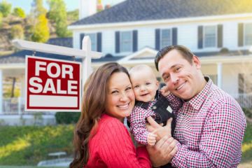 Young couple with baby next to house for sale sign Young couple with baby next to house for sale sign