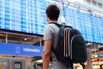 Young man looking at airport departures board Young man looking at airport departures board