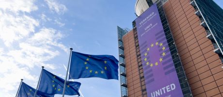 Several EU flags and the exterior view of the European Commission headquarters in Brussels,