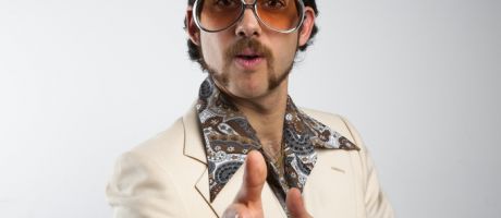 A man pulls a cheesy pose in 1970s clothing. Academics need to strike the right tone with their academic profiles if they want to attract PhD students.