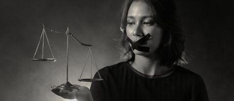 A woman wide tape over her mouth holds uneven scales of justice A woman wide tape over her mouth holds uneven scales of justice