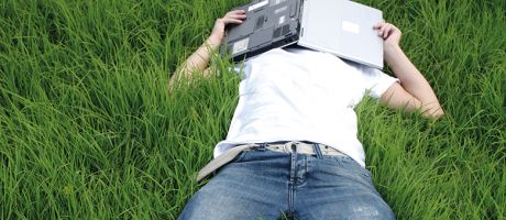A man lying in the grass covering his face with a laptop
