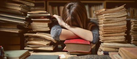 A young researcher with her head on her desk surrounded by piles of documents, illustrating early-career overwork