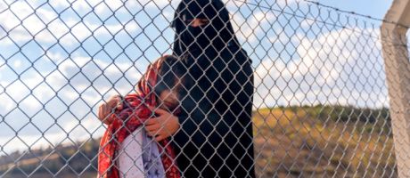 A refugee mother and her child behind a migrant camp fence A refugee mother and her child behind a migrant camp fence