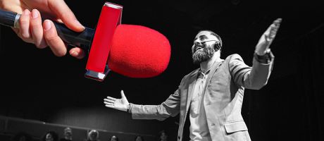 Man speaking to audience, with a large hand offering a microphone. To illustrate how speakers’ bureaux can boost academic authors’ profiles.
