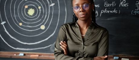 A black physics teacher stands in front of the blackboard