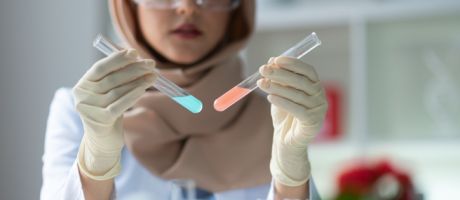 A woman holds up two test tubes containing differently coloured liquids