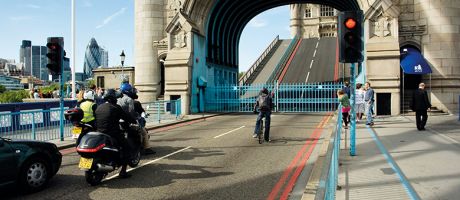 A cyclist, motorbikes and pedestrians wait as Tower Bridge in London is opened