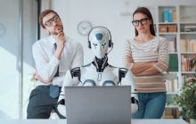 Humans look over the shoulder of a robot at a computer, symbolising human independent thought