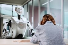 A woman writes while a robot wathes, symbolising AI tutoring A woman writes while a robot wathes, symbolising AI tutoring