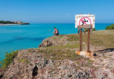 Man looking at the ocean next to a No Swimming sign