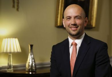 Ben Macpherson, a bald man wearing a suit, smiles at the camera 