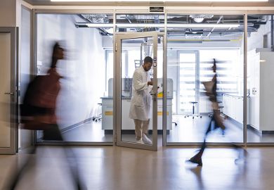 A chemical worker in a white coat stands between the doors of the faculty laboratory, students rush past him in the corridor A chemical worker in a white coat stands between the doors of the faculty laboratory, students rush past him in the corridor