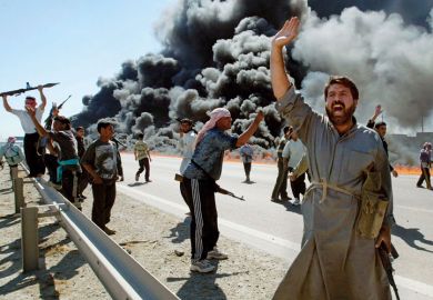 Armed Iraqi fighters standing on smoke-covered road