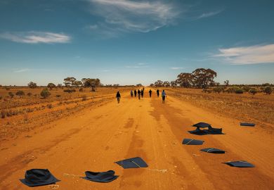 People walk down a dusty outback road, their abandoned mortar boards behind them