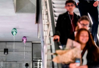 People travelling down escalator with balloons touching ceiling by artist Jeppe Hein. To illustrate cash-strapped universities deciding against raising fees for current students.