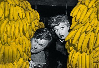 Man and woman peer out from behind bunches of bananas
