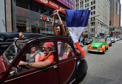 A woman holds a French flag as she rides in a parade of Citroen cars from the Greater New York Citroën and Velosolex Touring Club on Bastille Day in New York, USA. To illustrate a surge in interest in European jobs from US researchers.