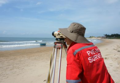 Binh Thuan, Viet Nam - October 21, 2014 Asian engineer work on Vietnamese beach, man looking in theodolite to survey sea level, measurement device set on tripod, Vietnam, Oct 21, 2013 Binh Thuan, Viet Nam - October 21, 2014 Asian engineer work on Vietnamese beach, man looking in theodolite to survey sea level, measurement device set on tripod, Vietnam, Oct 21, 2013