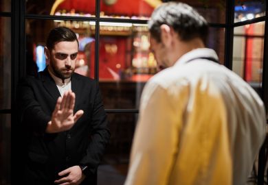A security guard blocks a doorway A security guard blocks a doorway, symbolising university access