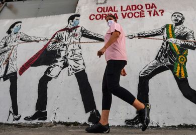 A woman passes by graffiti depicting Brazilian President Jair Bolsonaro pulling a rope against health workers with the question "Which side of the rope are you on?", Brazil, 2020. To illustrate ‘political shocks’ hitting women’s representation in science.