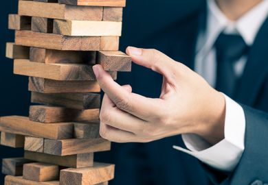 Businessman carefully removing wooden block from tower Businessman carefully removing wooden block from tower