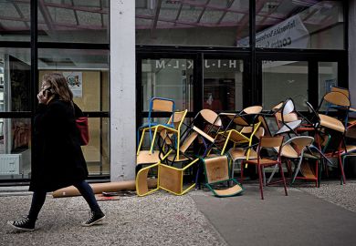 A student walks past a pile of chairs blocking a door of the Bordeaux Montaigne University, in Pessac