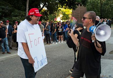 A man holds a sign that says "For Charlie" as people protest outside the "American Comeback Tour" event at Northrop Auditorium on the University of Minnesota campus on 22 September, 2025. The event was held after the assassination of Charlie Kirk.