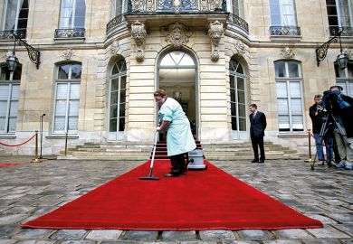 A woman vacuums a red carpet outside a posh building A woman vacuums a red carpet outside a posh building
