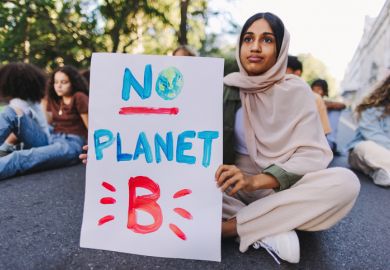 A climate protester sits in the road with "no planet B" sign