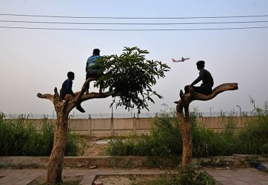 People climb trees to watch the take off of an airplane along a highway, outside Indira Gandhi International Airport in New Delhi, India. To illustrate that setting up a branch campus in India may be costly, limited in reach and difficult to scale.