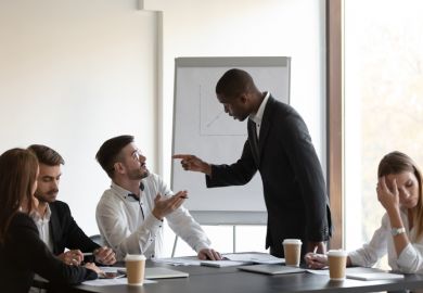 People gesticulate at each other in a business meeting, symbolising conflict within business schools
