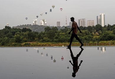 Man reflected in water in Asian city on the cover of 24 June 2021 issue of Times Higher Education magazine
