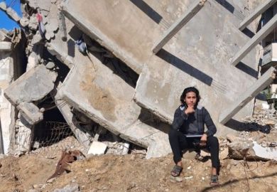A young student in Gaza sitting near the ruins of his home 