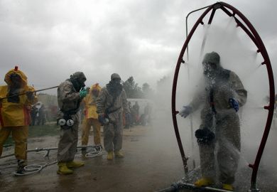 A person in a chemical protection suit walks through a decontamination shower as another is washed down during a mock chemical attack. To illustrate researchers might need to demand retraction of their own papers to decontaminate scientific literature.