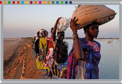 A group of women walk along a dyke protecting Internally Displaced Persons (IDPs), and their host community, from further flooding in Bentiu, South Sudan, 2023. Climate change has divided South Sudan into land that is experiencing flood or drought.