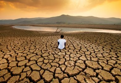 A boy sits on the cracked bed of a drying lake