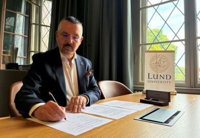 Lund vice-chancellor Erik Renstrom sitting at a desk, signing a document, with a sign that says Lund University on the desk