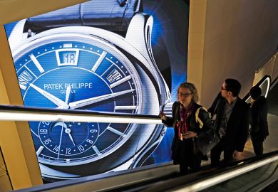 Visitors traveling on an escalator pass a Patek Philippe luxury wristwatch advertisement. To illustrate that there has been an increase in the number of staff paid more than £100,000 at Russell Group universities.