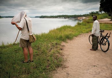 A man looks on in amusement as Ashley Kirk-Spring, a British scientist studying flies beside the Lomami River in DRC, has to put his head right into the net he has caught them in to examine them closely A man looks on in amusement as Ashley Kirk-Spring, a British scientist studying flies beside the Lomami River in DRC, has to put his head right into the net he has caught them in to examine them closely