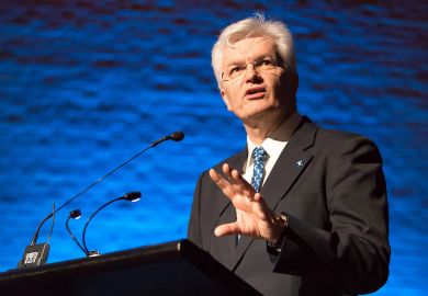 A man with grey hair and wearing a suit speaks at a podium 