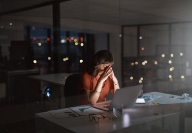 A woman looking stresed while working on a laptop in a dimly lit room