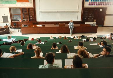 A wide lecture hall with students in tiered seating with green desks